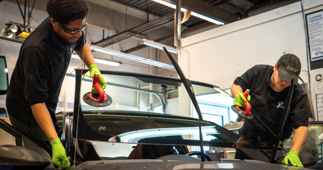 Glass installers setting a new windshield into a vehicle